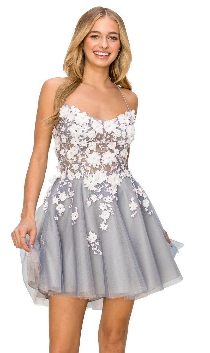 A woman smiles as she stands against a plain background, wearing the Backless Sheer-Waist Floral Homecoming Dress 8053J—a short, sleeveless light blue dress adorned with white 3-D flowers.